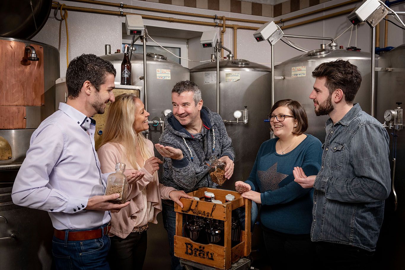 Gruppe von Menschen in einer Brauerei mit Bierflaschen und Zutaten.
