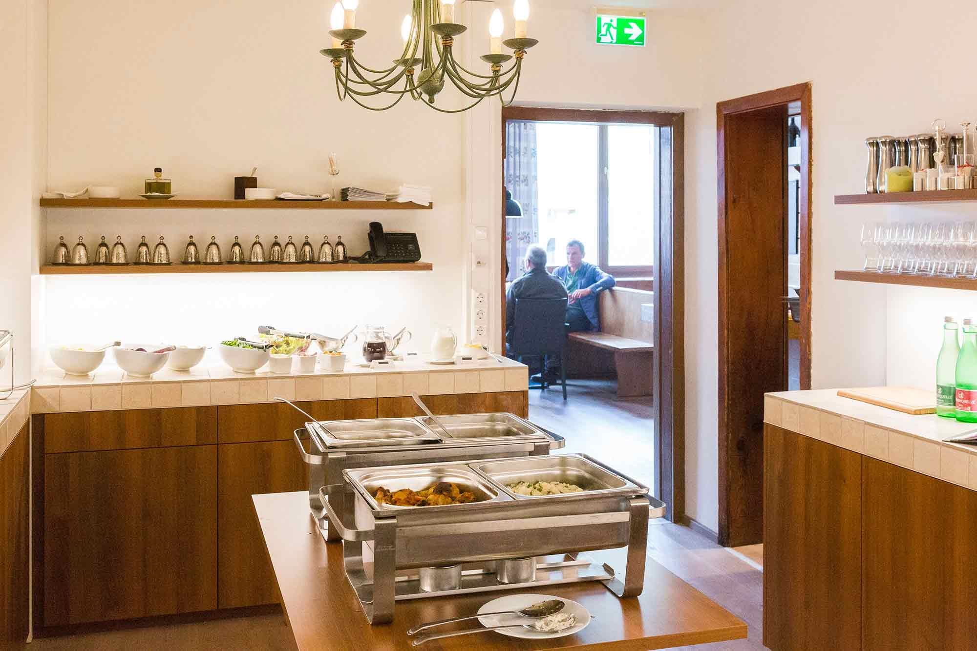 Buffetraum mit Speisen und Blick in ein angrenzendes Zimmer mit zwei Personen.