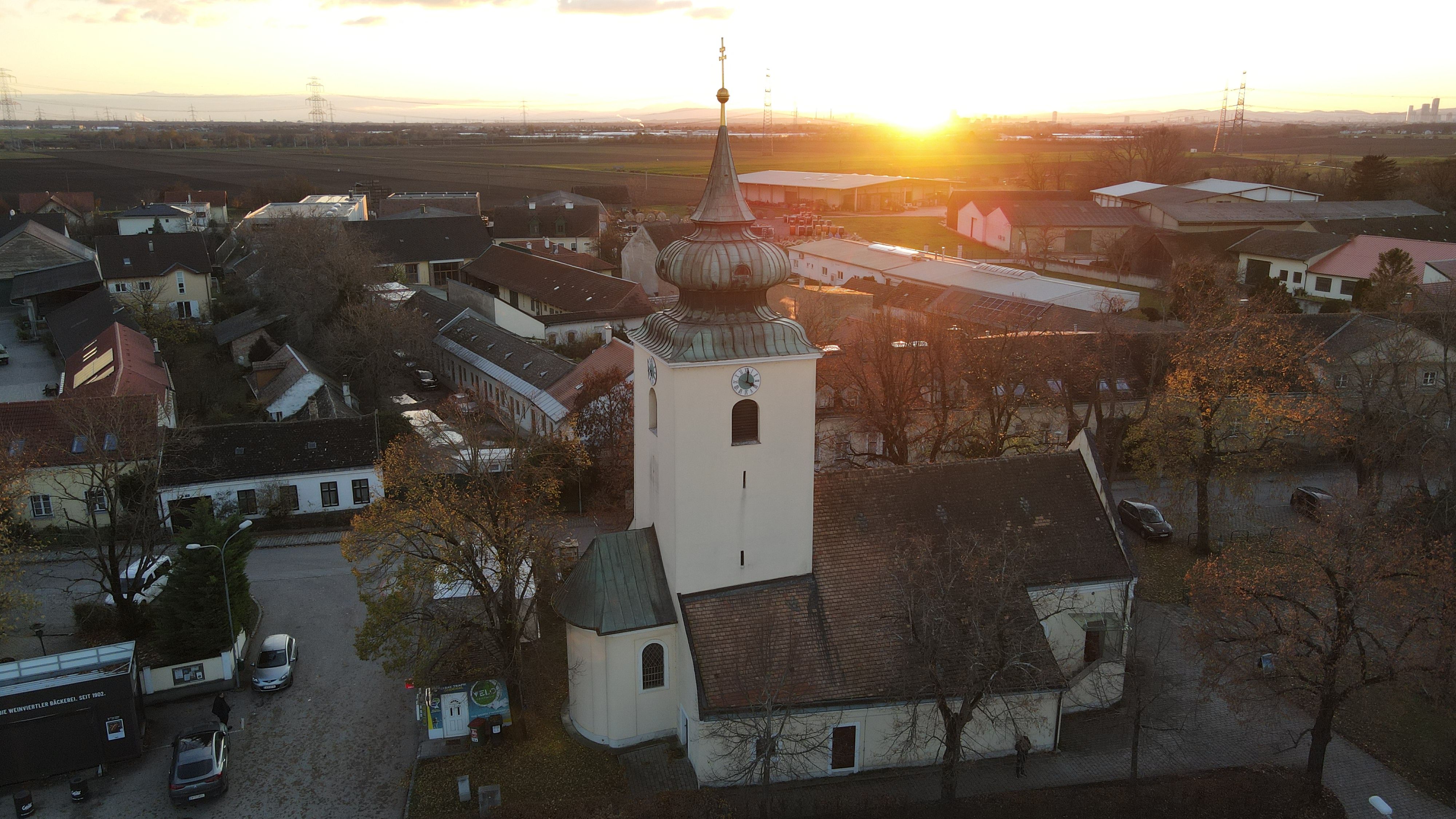 Kirche Raasdorf mit Turm und Zwiebeldach bei Sonnenuntergang, umgeben von Häusern und Feldern.