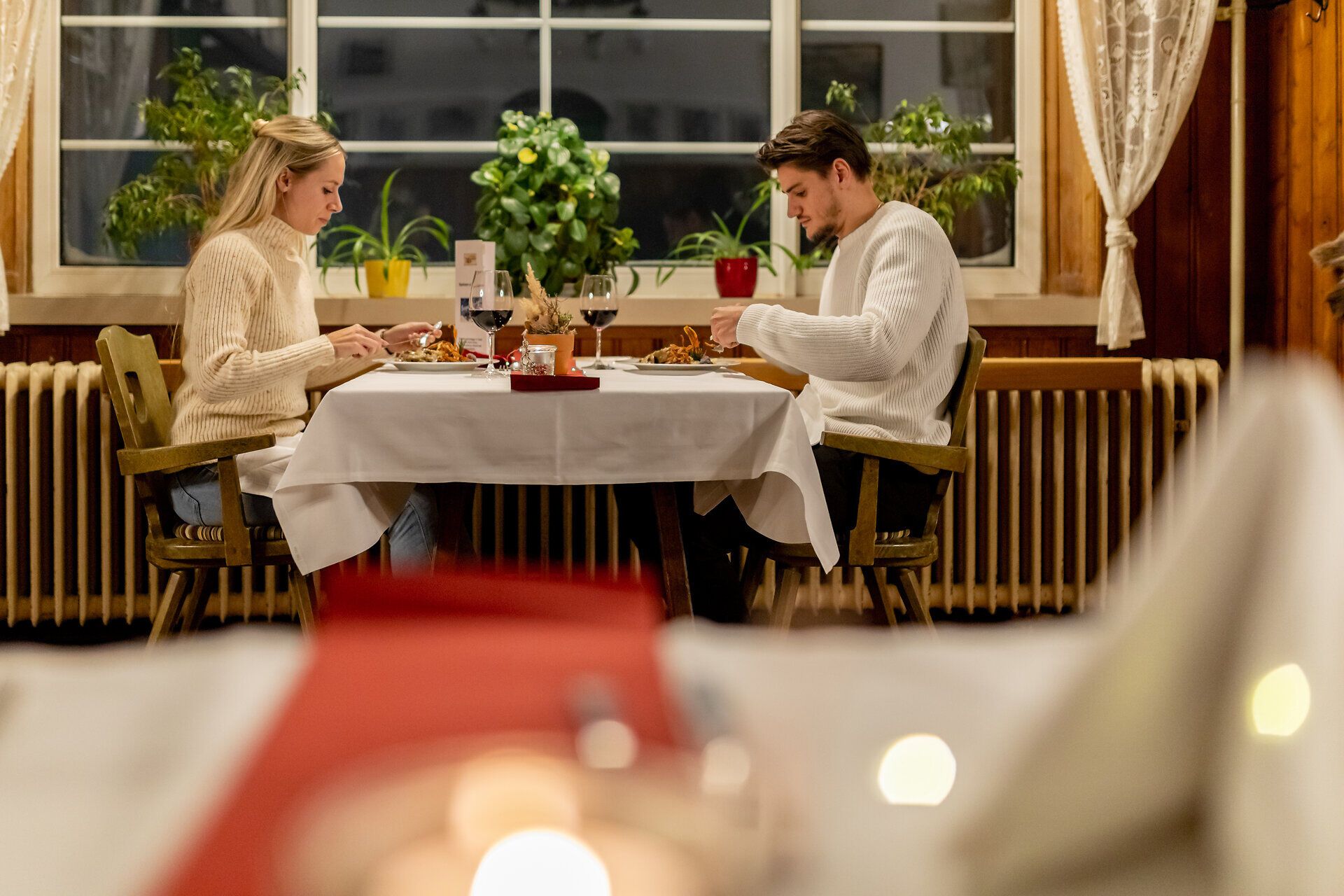 Paar sitzt sich in gemütlichem Raxalm-Berggasthof gegenüber und isst gemeinsam bei Kerzenlicht.