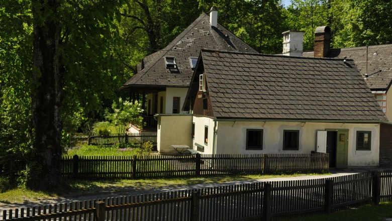 Ein traditionelles G&auml;stehaus mit Holzzaun und Garten, umgeben von B&auml;umen.