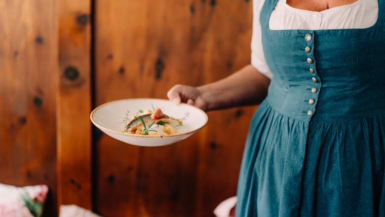 Frau in traditioneller Tracht serviert ein Gericht auf einem Teller.