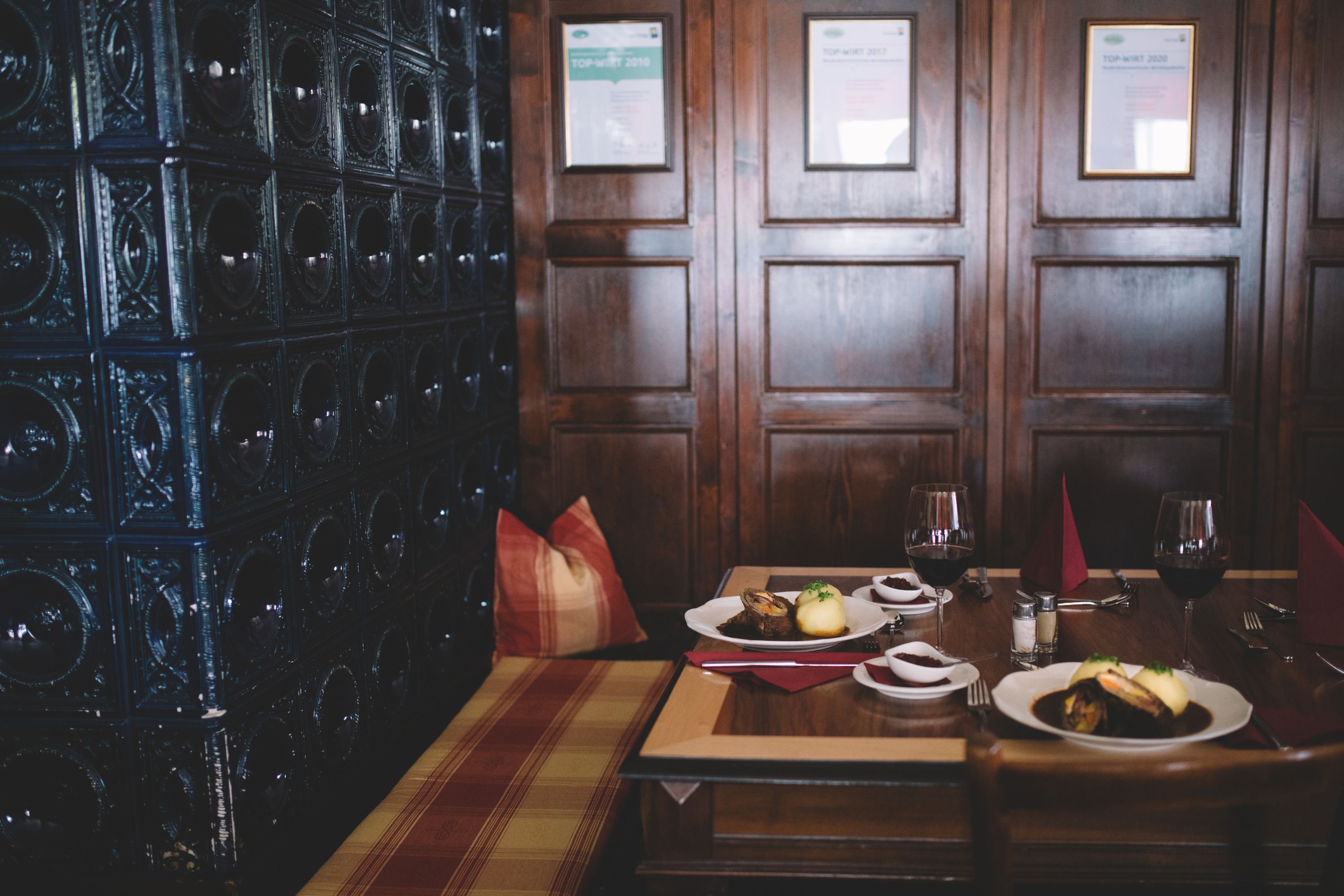 Gemütliche Gaststube mit Holzwänden, gedecktem Tisch und Kachelofen.