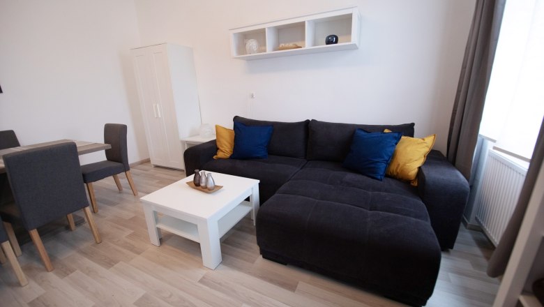 Moderner Wohnbereich mit grauem Sofa, bunten Kissen, wei&szlig;em Couchtisch und Esstisch mit St&uuml;hlen.