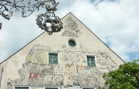 Fassade eines Hauses mit Sgraffito-Kunstwerk und dekorativem Metallschild.