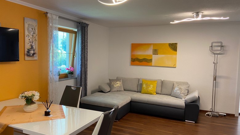 Wohnküche mit grauer ausziehbarer Couch, Esstisch und Dekorationen.