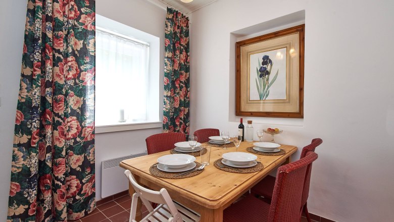 Ein Esstisch mit vier Gedecken, roten Stühlen und einem Blumenbild an der Wand.