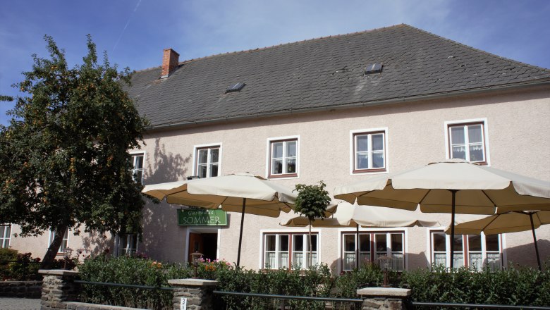 Ein traditionelles Gasthaus mit Sonnenschirmen und einem Baum im Vordergrund.