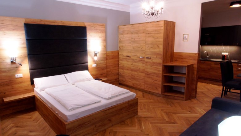 Modernes Apartment mit Holzmöbeln, Doppelbett, Schrank, Kronleuchter und Küchenzeile.
