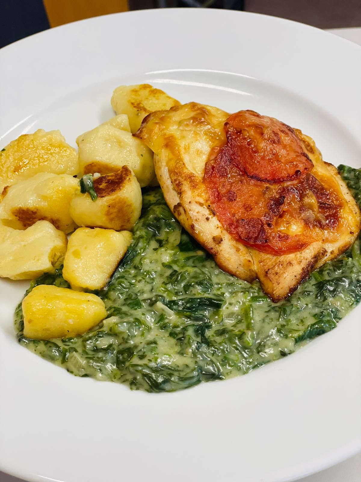 Teller mit Gnocchi, cremigem Spinat und überbackenem Hähnchen mit Tomatenscheibe.