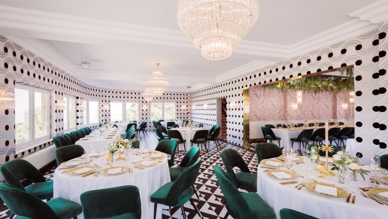 Elegantes Restaurant mit runden Tischen, gr&uuml;nen St&uuml;hlen und Kronleuchtern.