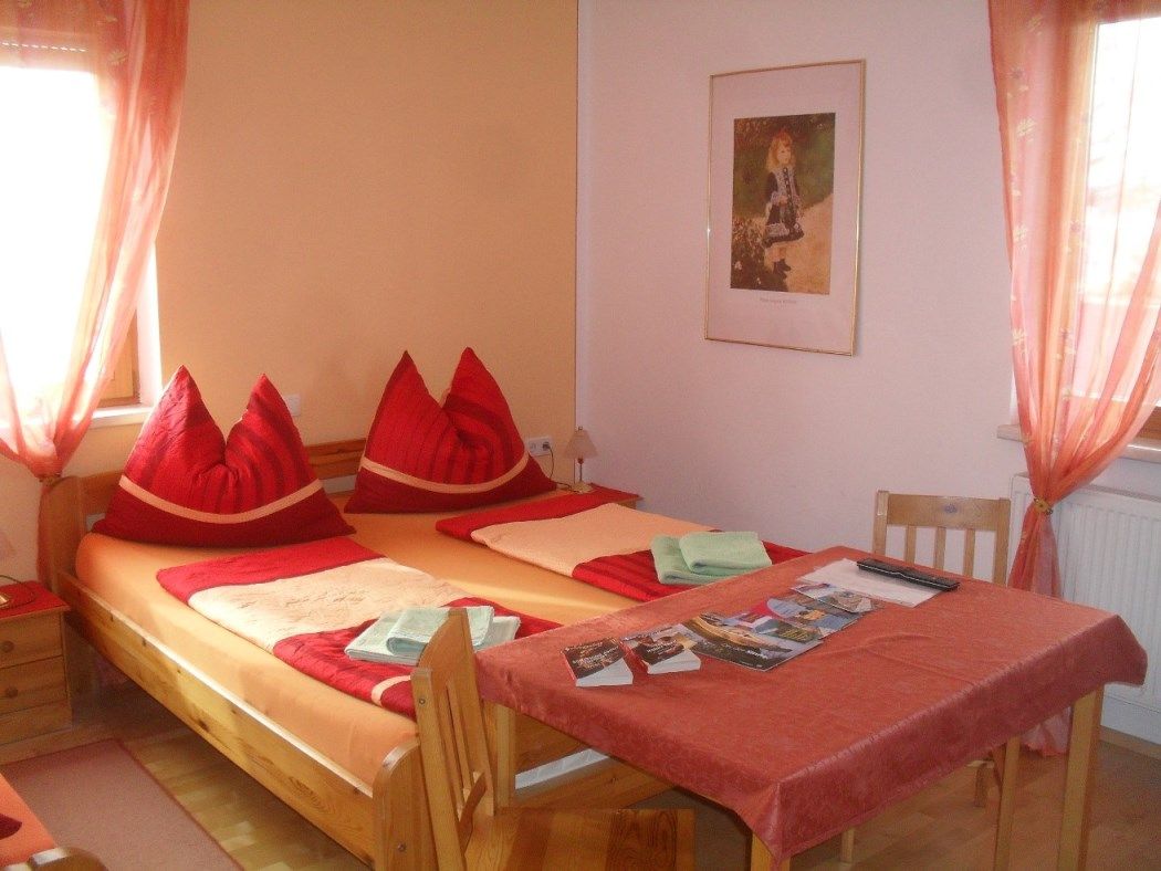 Gemütliches Schlafzimmer mit Doppelbett, roten Kissen und Tisch mit Broschüren.