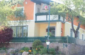 Ein zweistöckiges Haus mit orange-gelber Fassade, grünem Zaun und Garten.