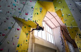 Person klettert an einer Indoor-Kletterwand mit bunten Griffen.