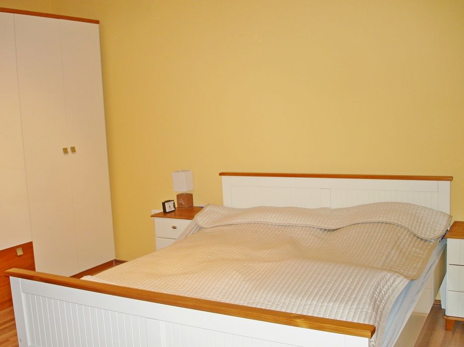 Schlafzimmer mit Doppelbett, gelber Wand und weißem Kleiderschrank.