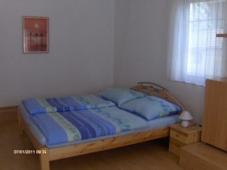 Ein einfach eingerichtetes Schlafzimmer mit einem Doppelbett, einem Nachttisch und einem Fenster mit Vorhängen.