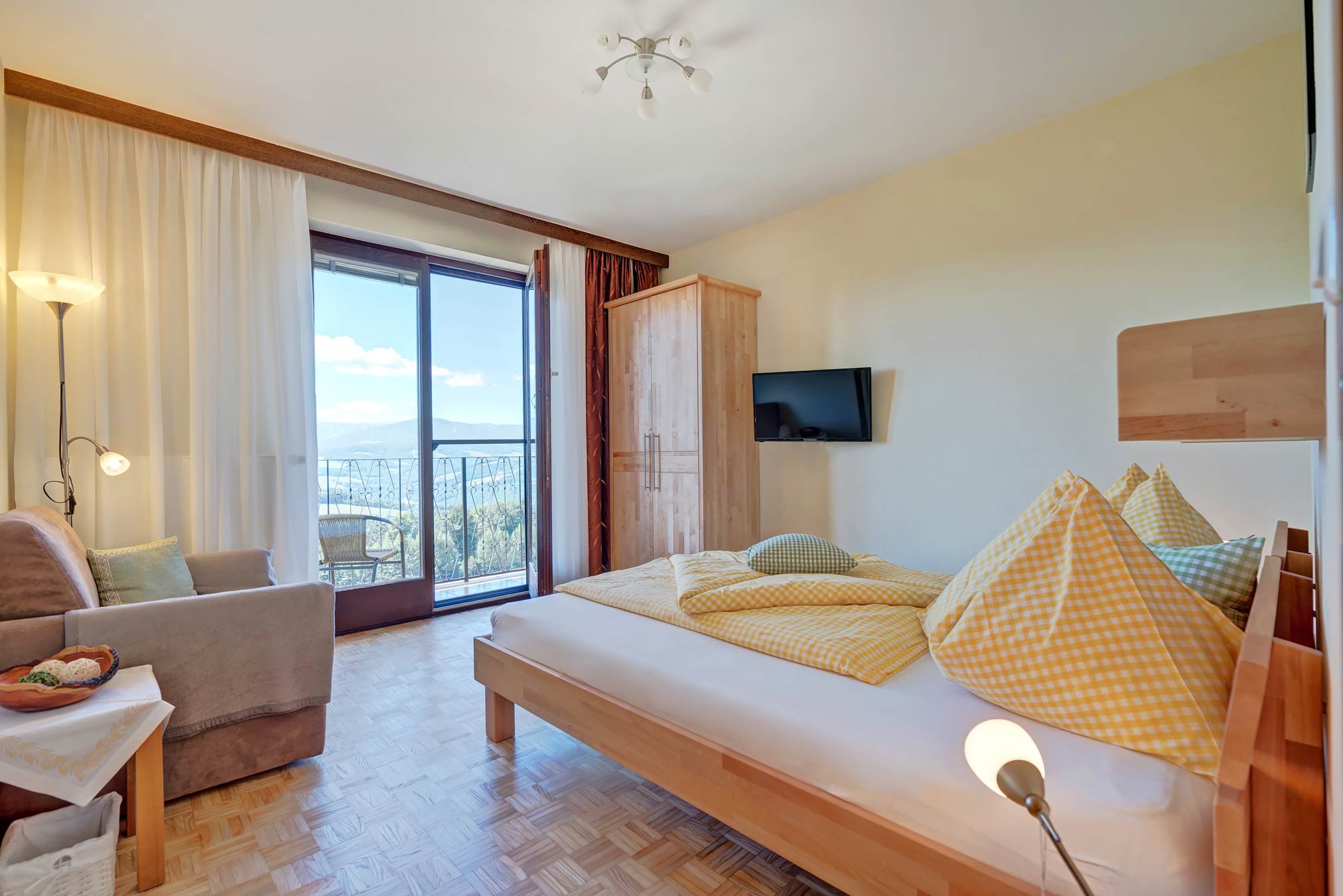 Helles Schlafzimmer mit Bett, Sofa, Schrank und Balkon mit Aussicht.