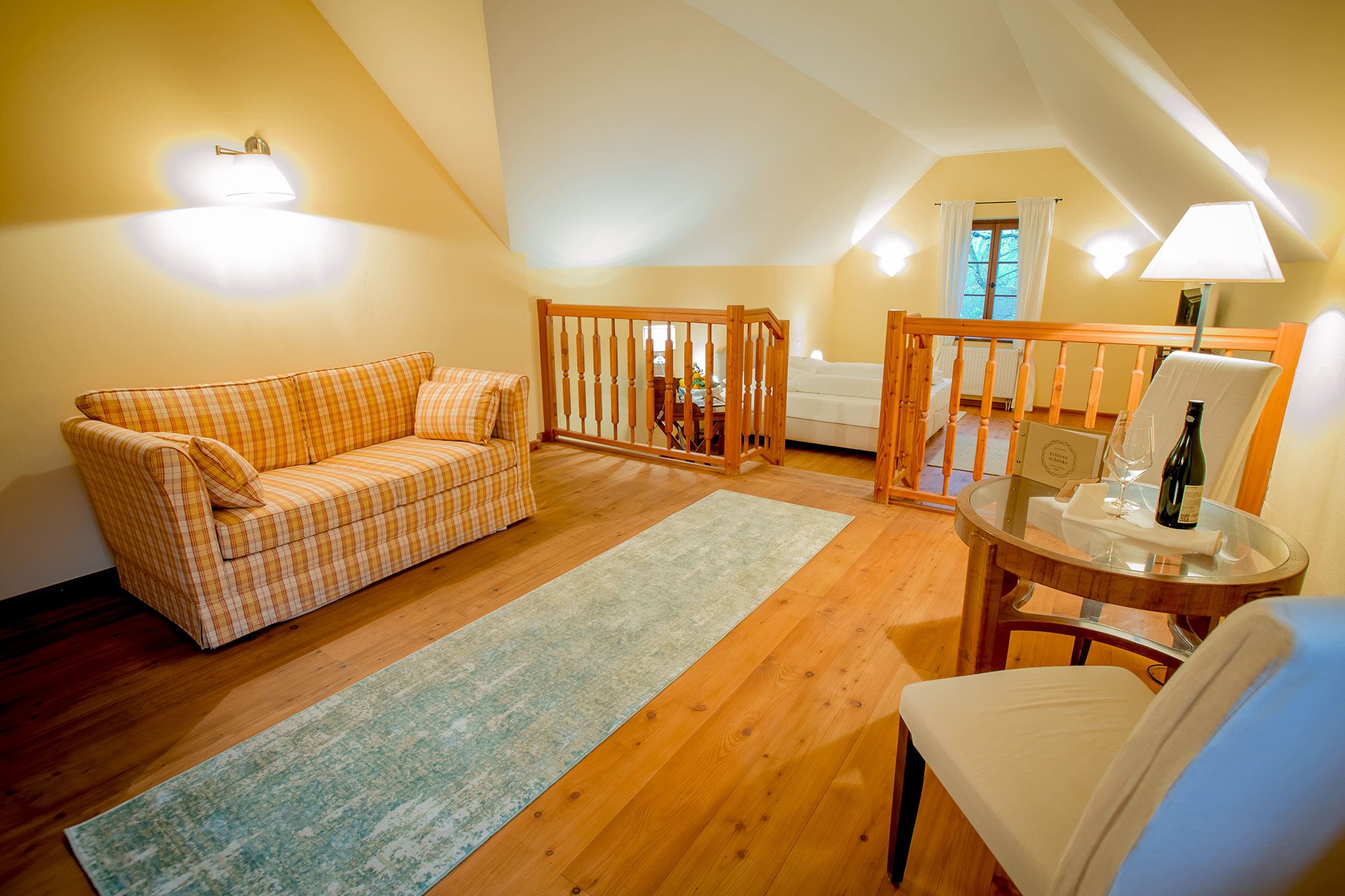 Gemütliches Zimmer mit Sofa, Tisch und Stuhl, Holzboden und Geländer.