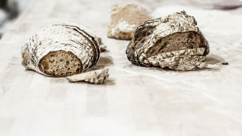 Zwei Laibe Brot auf einem Holztisch, teilweise geschnitten.