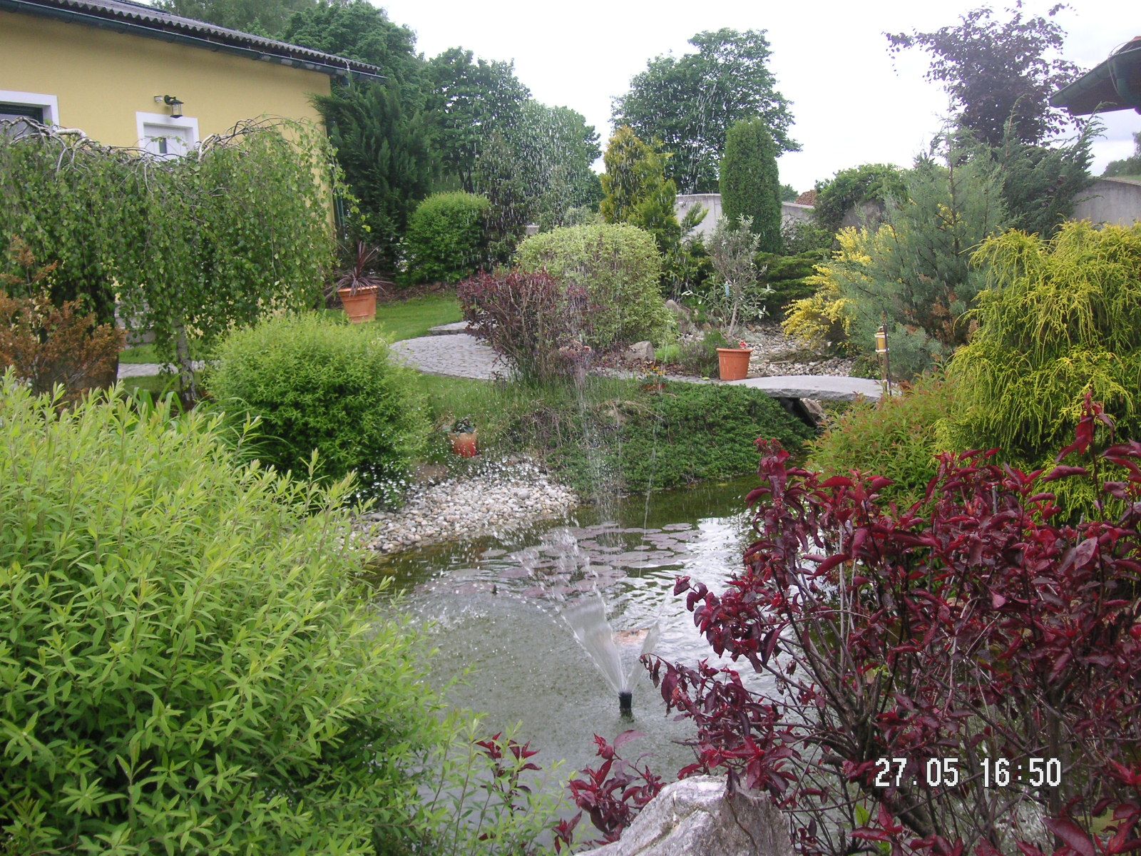 Ein gepflegter Garten mit Teich, Springbrunnen und üppiger Vegetation.