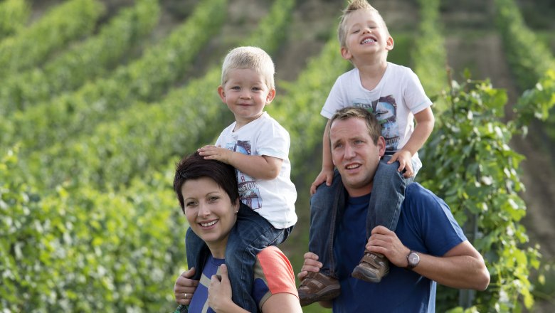 Familie in einem Weinberg, zwei Kinder auf den Schultern der Eltern.