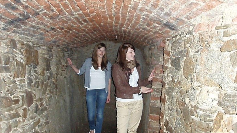 Zwei Frauen in einem schmalen, gemauerten Tunnel mit Ziegeldecke.