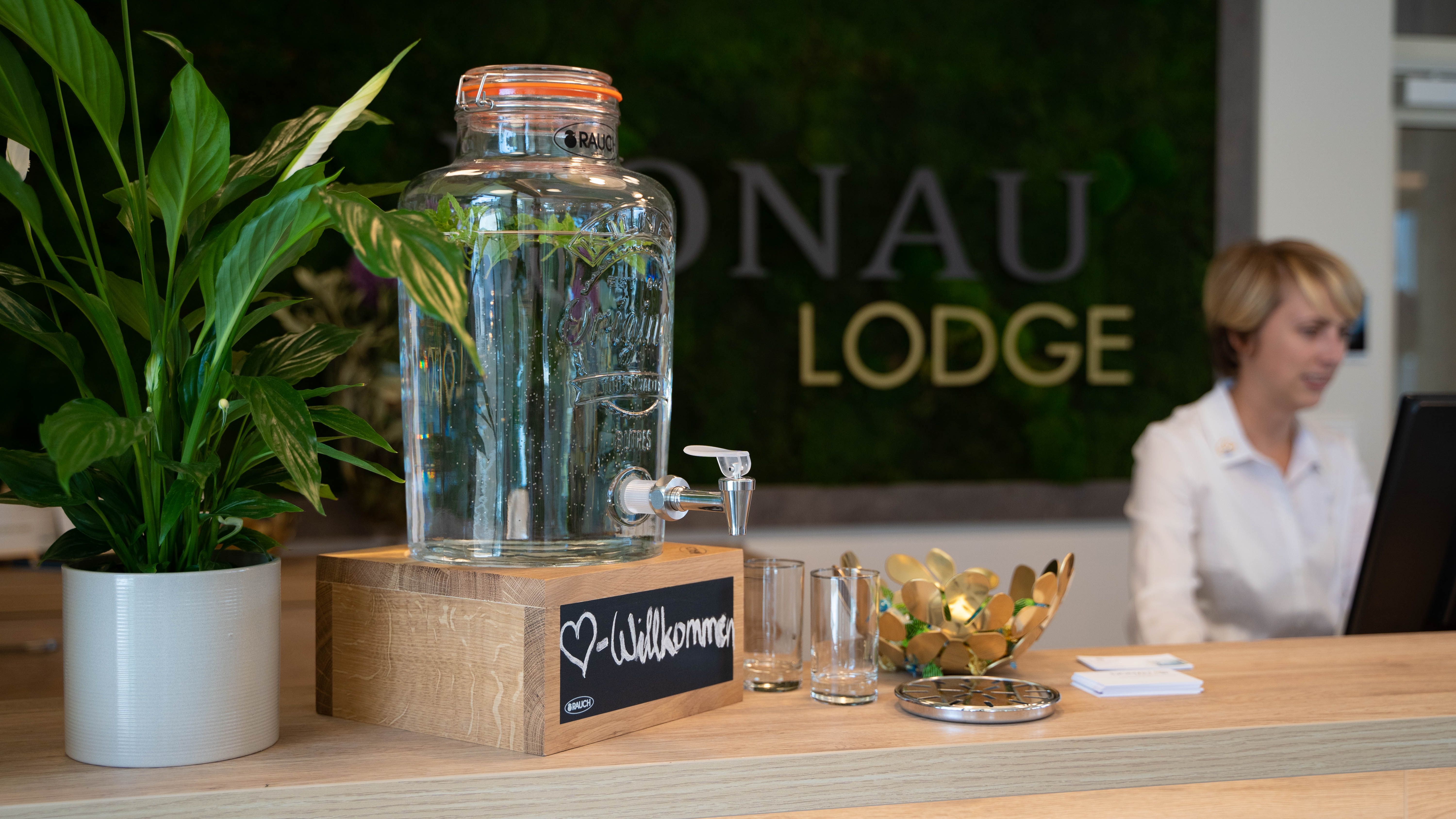 Rezeption mit Wasserspender, Pflanzen und Mitarbeiterin am Computer.