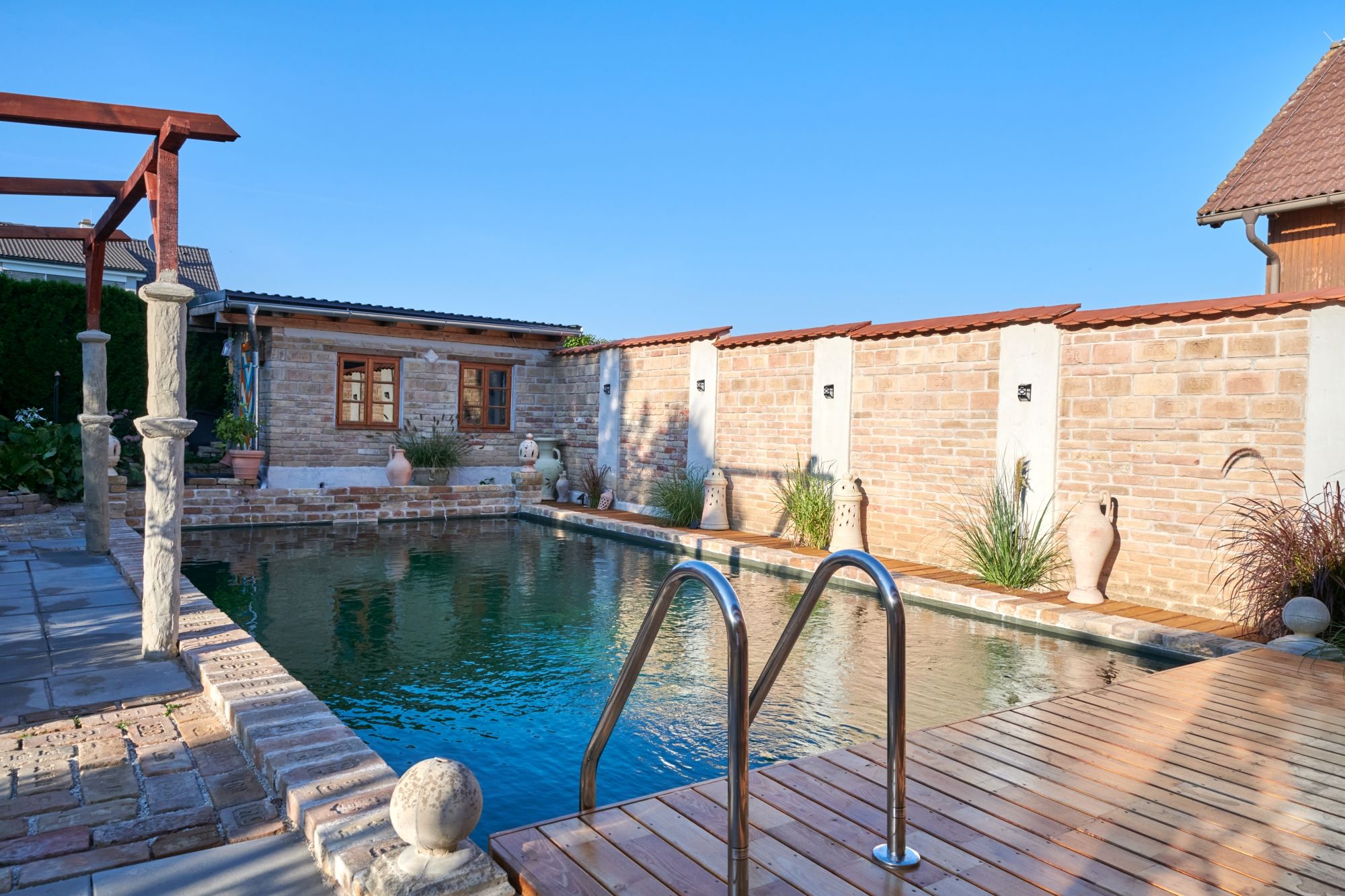 Ein kleiner Pool mit Holzdeck und Backsteinmauern im Hintergrund.