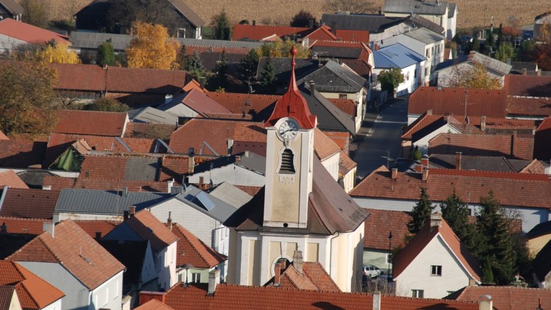 Luftaufnahme der Pfarrkirche Getzersdorf mit umliegenden Häusern und Feldern im Herbst.