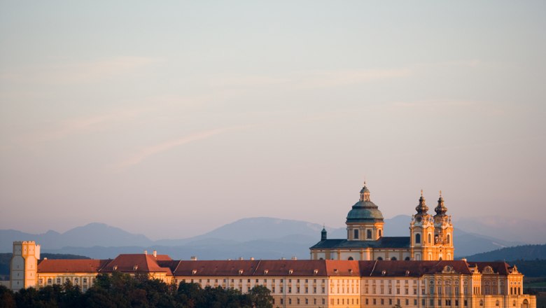 Stift Melk in Österreich bei Sonnenuntergang mit Bergen im Hintergrund.