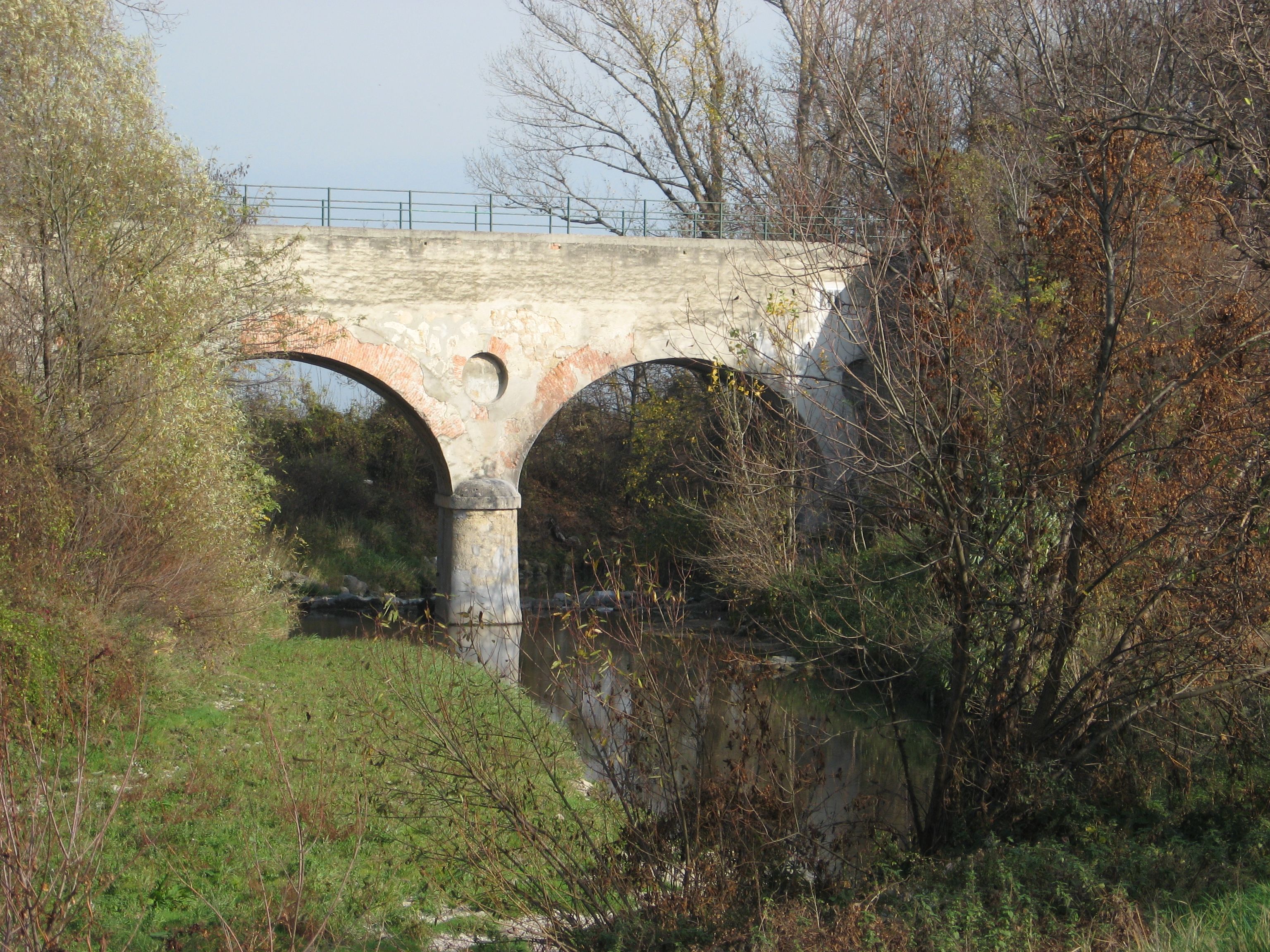 Alte Steinbrücke über einen kleinen Fluss, umgeben von Bäumen im Herbst.