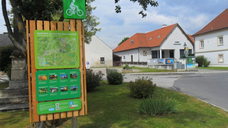 Radstartplatz-Tafel in Walpersbach mit Karte und Informationen, umgeben von Geb&auml;uden und B&auml;umen.
