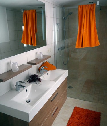 Modernes Badezimmer mit Doppelwaschbecken, gro&szlig;er Spiegel, Dusche und orangefarbenen Akzenten.