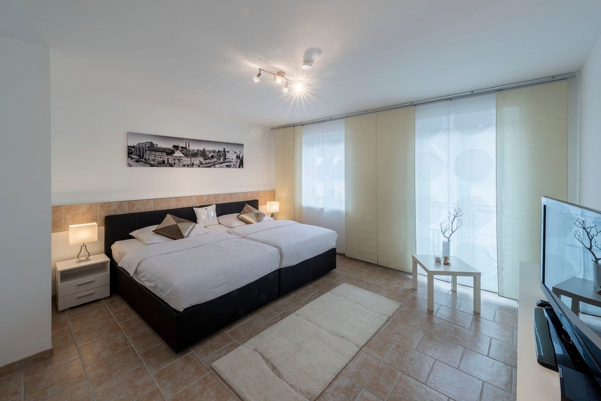 Modern eingerichtetes Schlafzimmer mit zwei Betten, Nachttischen, einem Bild an der Wand und einem Fernseher.