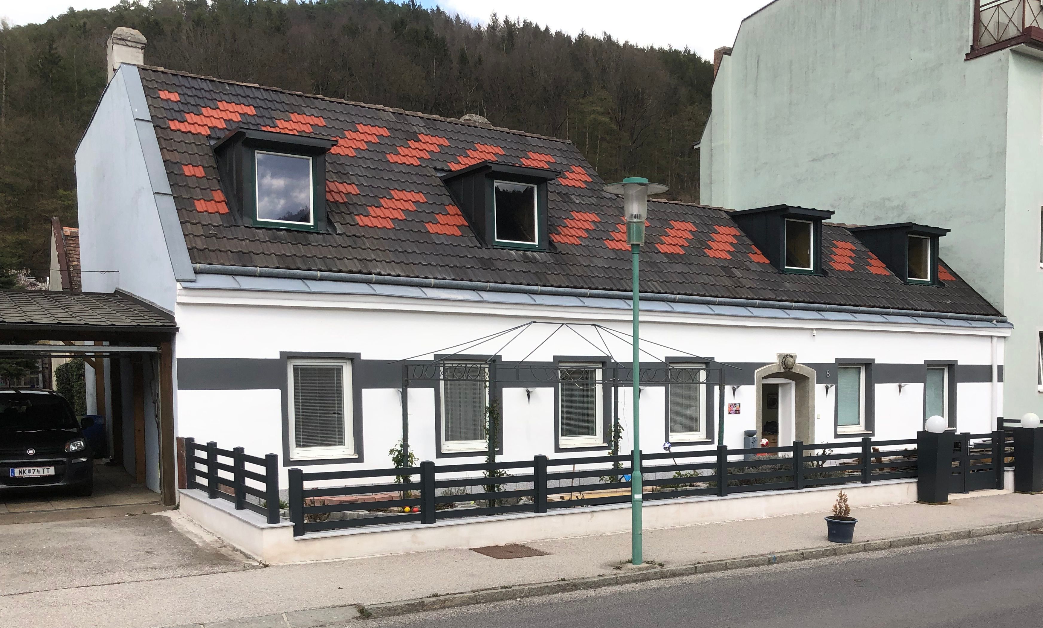 Ansicht eines weißen Hauses mit schwarzem Zaun und Dachfenstern.