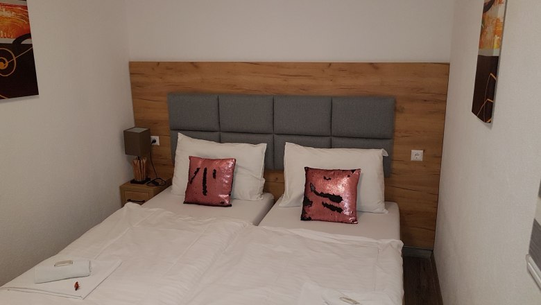 Doppelzimmer mit zwei Einzelbetten, grauem Kopfteil, rosa Pailletten-Kissen und wei&szlig;er Bettw&auml;sche.