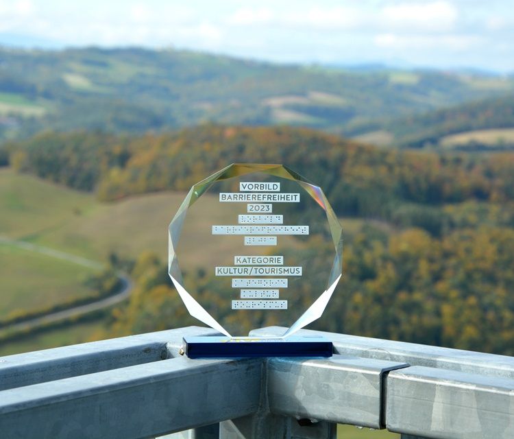 Eine Auszeichnung für Barrierefreiheit 2023 steht auf einem Geländer mit Landschaft im Hintergrund. Die Aussichtsplattform ist mit einem Aufzug erreichbar.