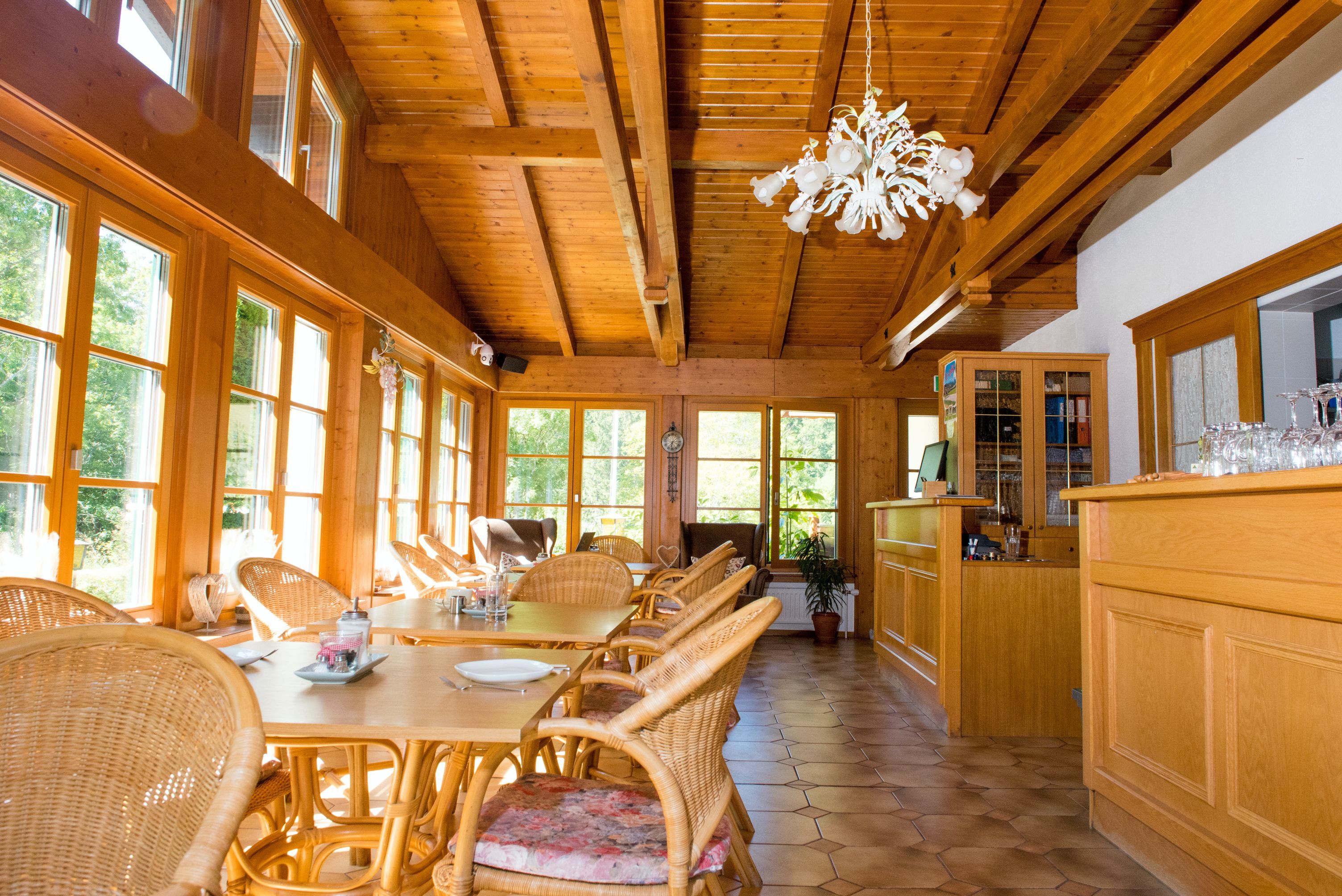 Ein heller Frühstücksraum mit Holzmöbeln, großen Fenstern und einem Kronleuchter.