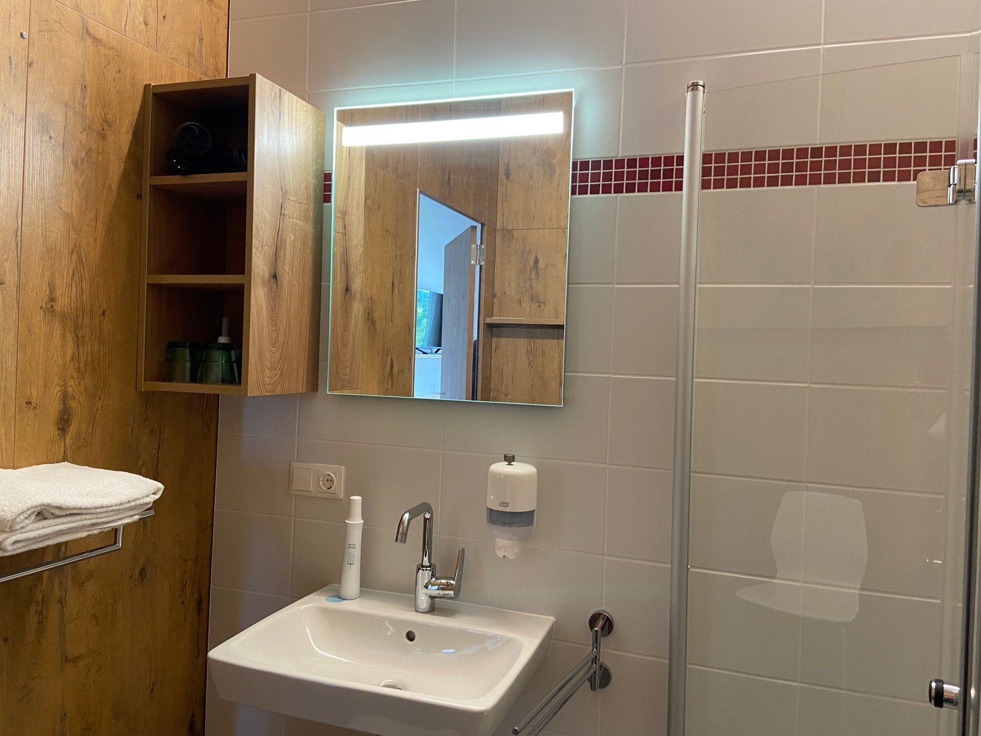 Modernes Badezimmer mit Waschbecken, Spiegel, Holzregal und Duschkabine.