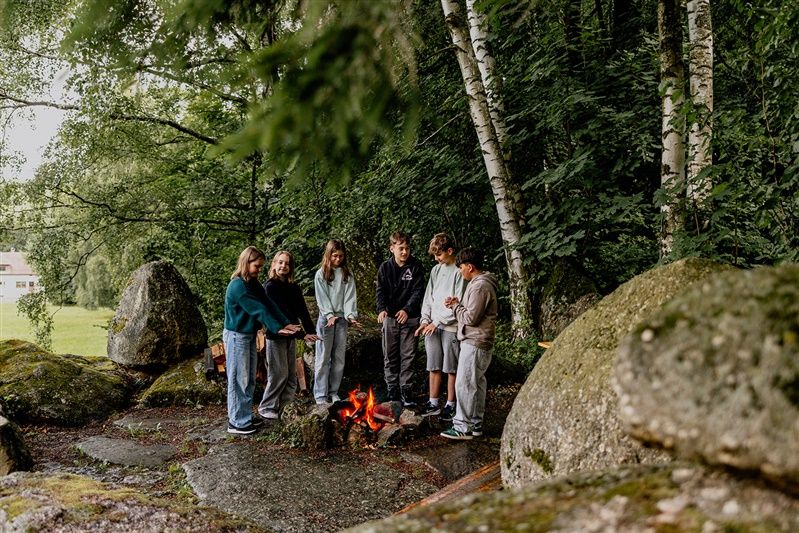 Gruppe von Jugendlichen steht um ein Lagerfeuer im Wald.