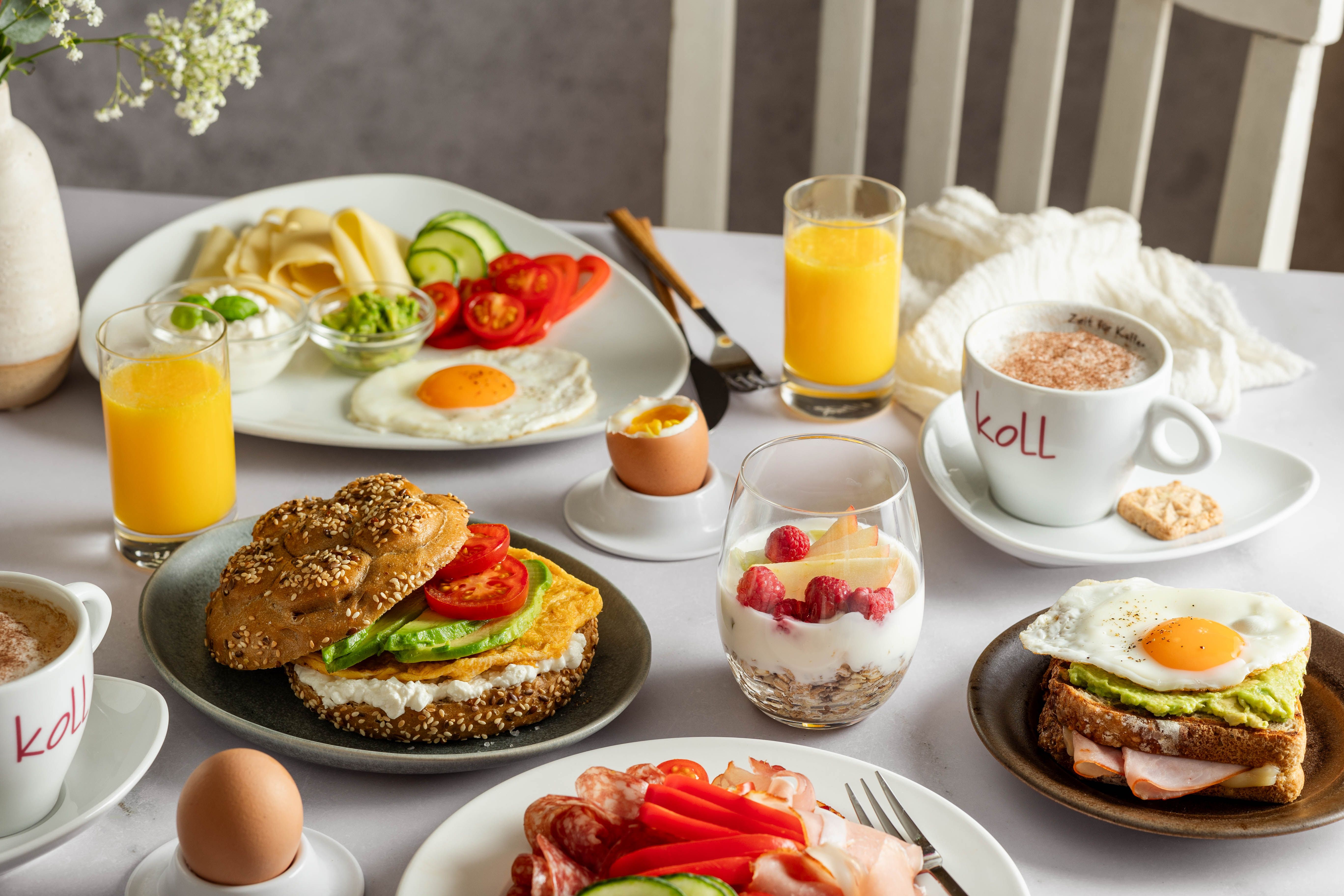 Frühstückstisch mit Brötchen, Aufschnitt, Spiegelei, Joghurt mit Beeren, Orangensaft und Kaffee.