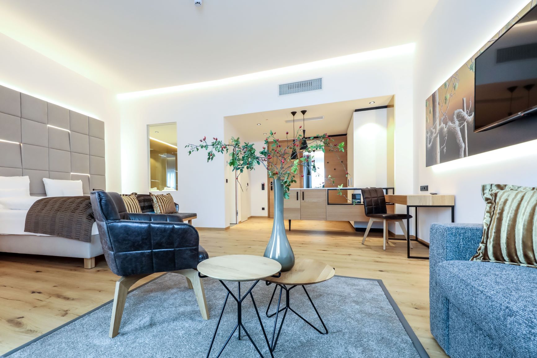 Modern eingerichtetes Hotelzimmer mit Bett, Sesseln, Tisch und Dekoration.