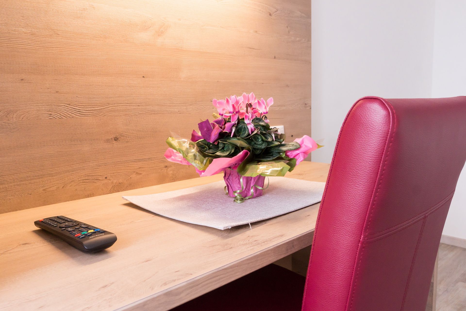 Ein Schreibtisch mit einer Fernbedienung, einem Blumenstrauß und einem roten Stuhl.