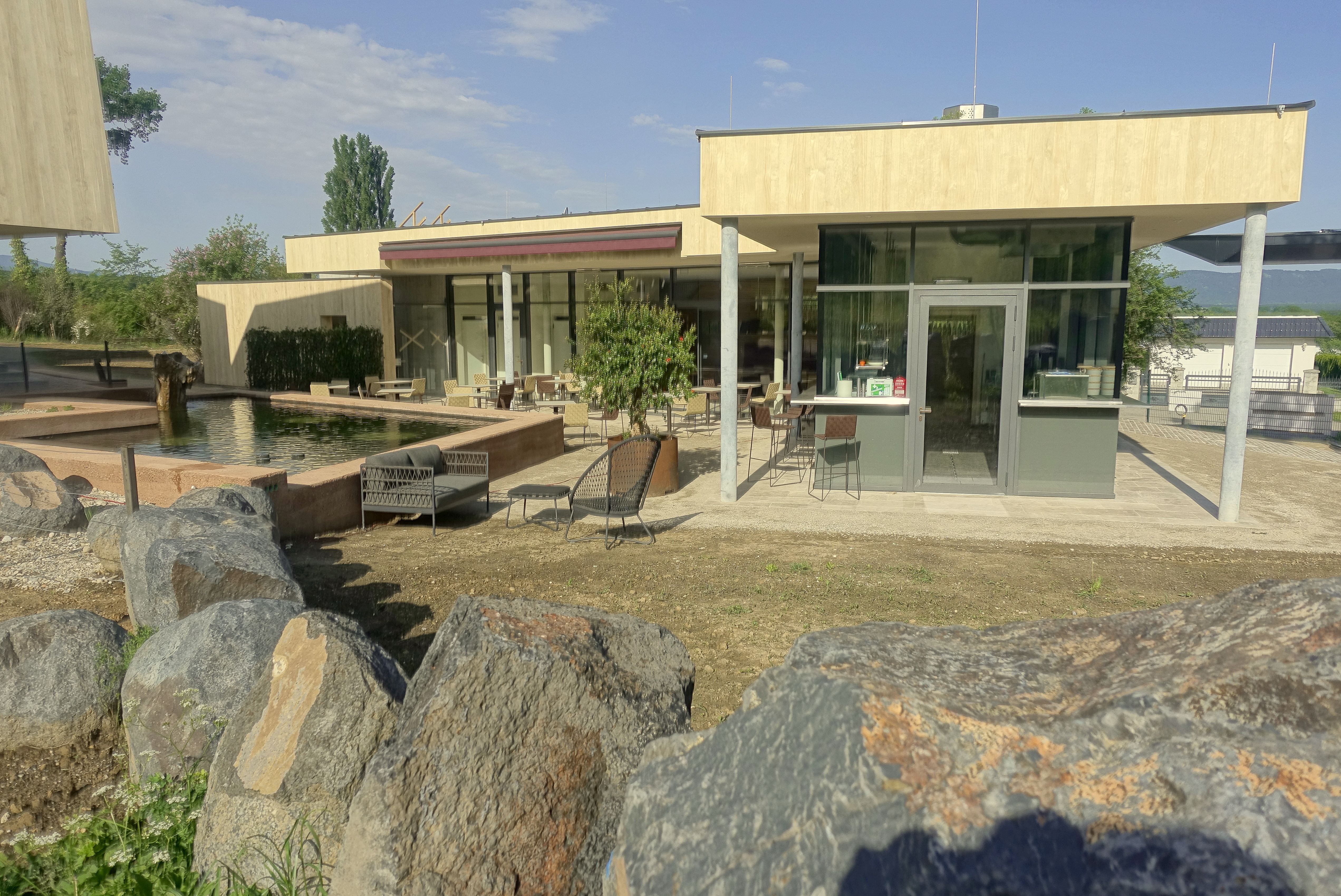 Moderne Veranda mit Glasfront und Sitzbereich, umgeben von Felsen und einem Teich.