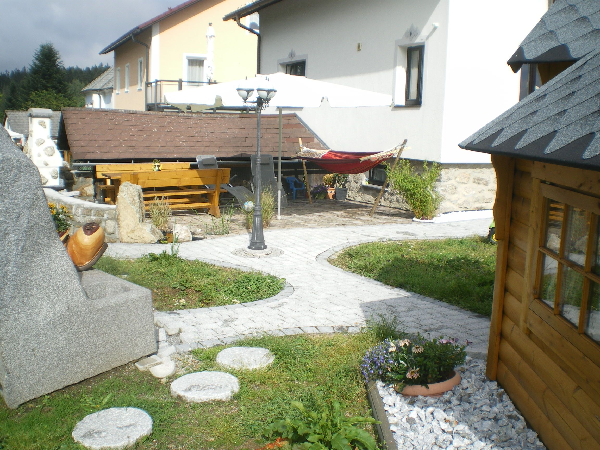 Garten mit Steinen, Holzhaus, Tisch, Hängematte und Sonnenschirm.
