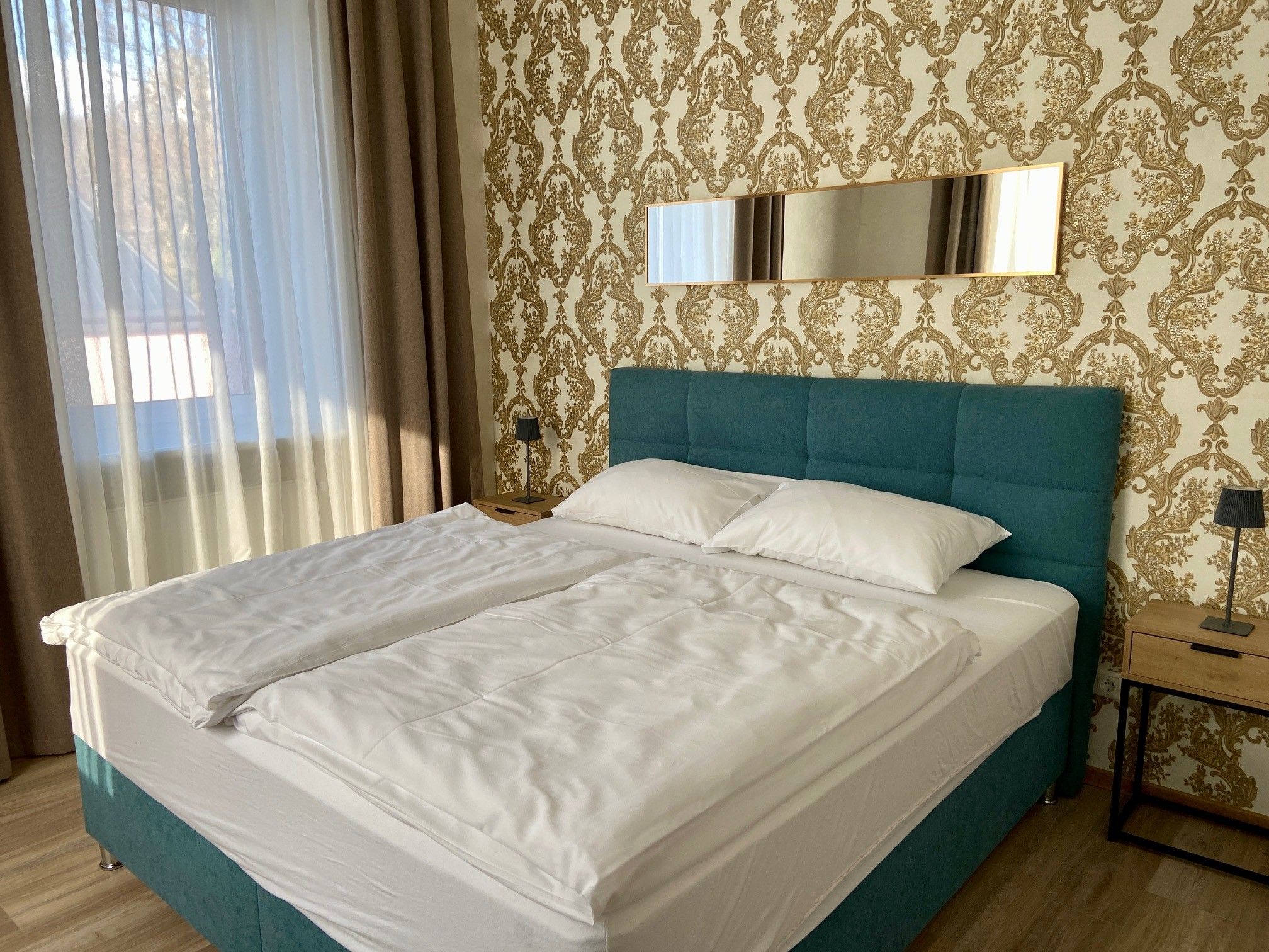 Ein stilvoll eingerichtetes Schlafzimmer mit einem großen Bett, blauen Kopfteil und goldener Tapete.