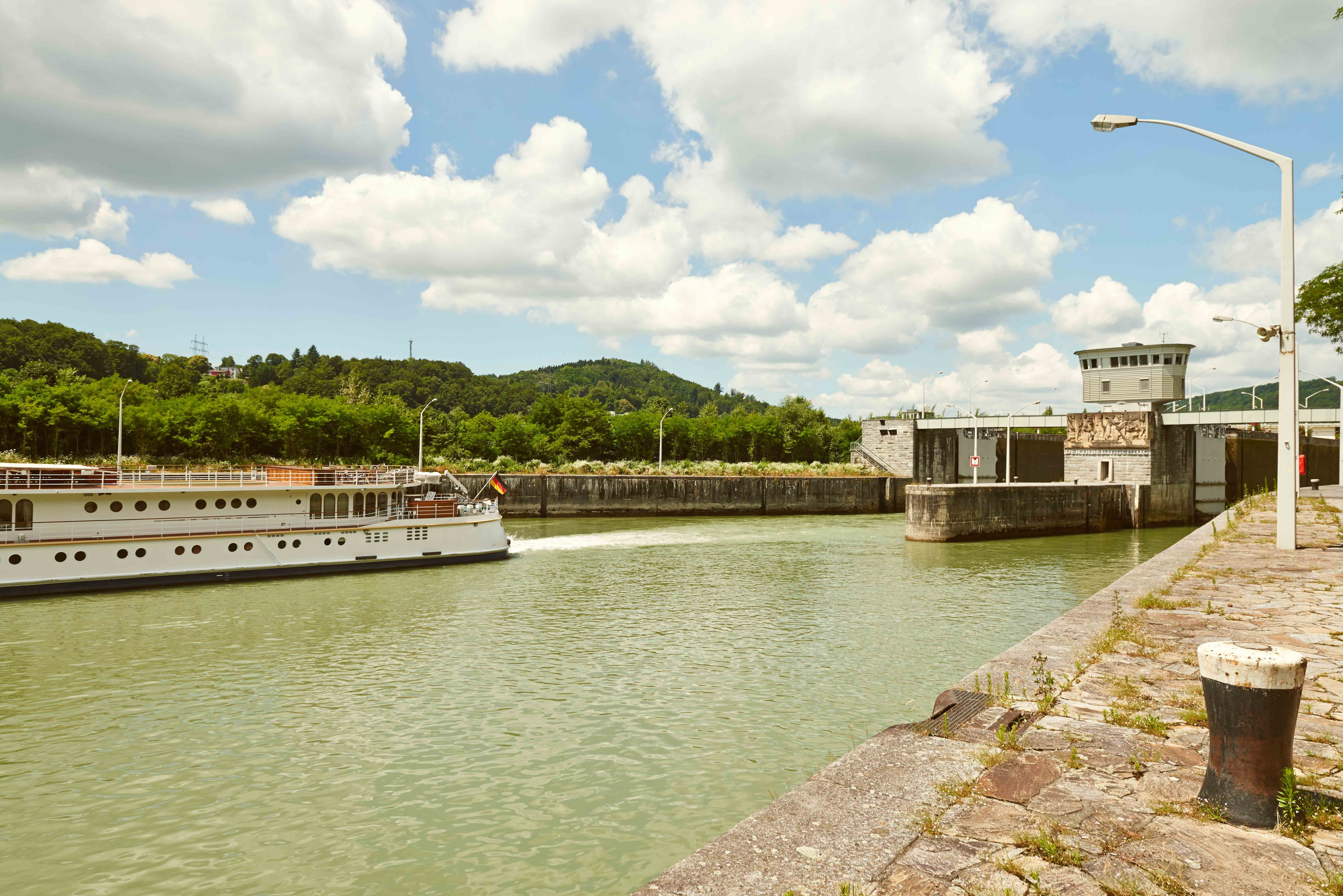 Ein Schiff fährt durch eine Schleuse am Donaukraftwerk Ybbs-Persenbeug, umgeben von grüner Landschaft und bewölktem Himmel.