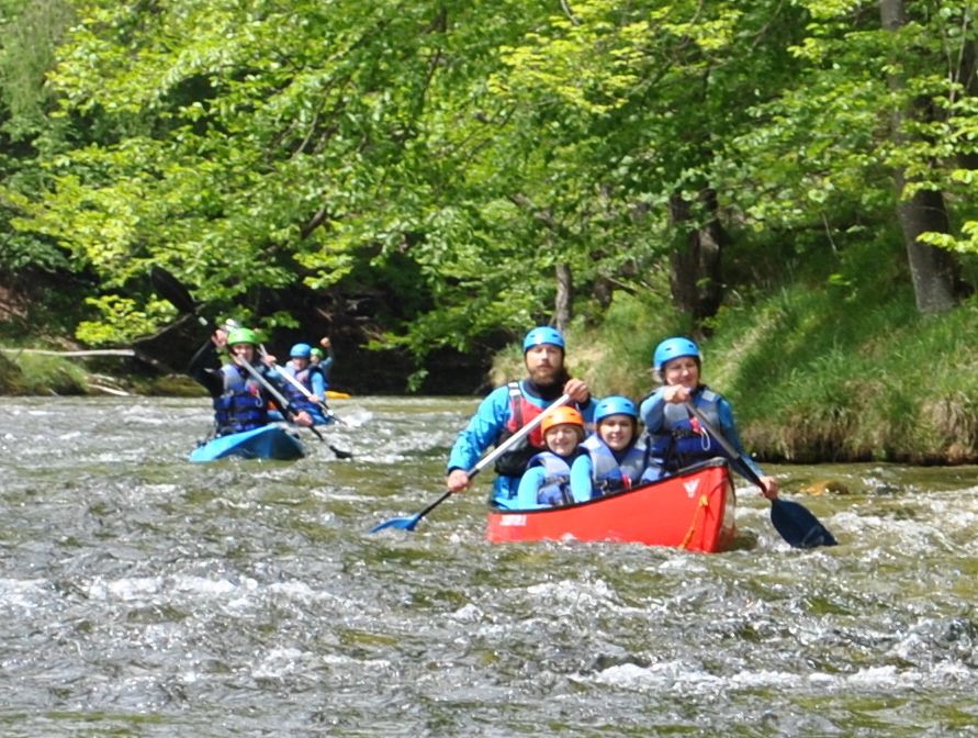 Menschen in Kanus paddeln auf einem Fluss in einer grünen Waldlandschaft.
