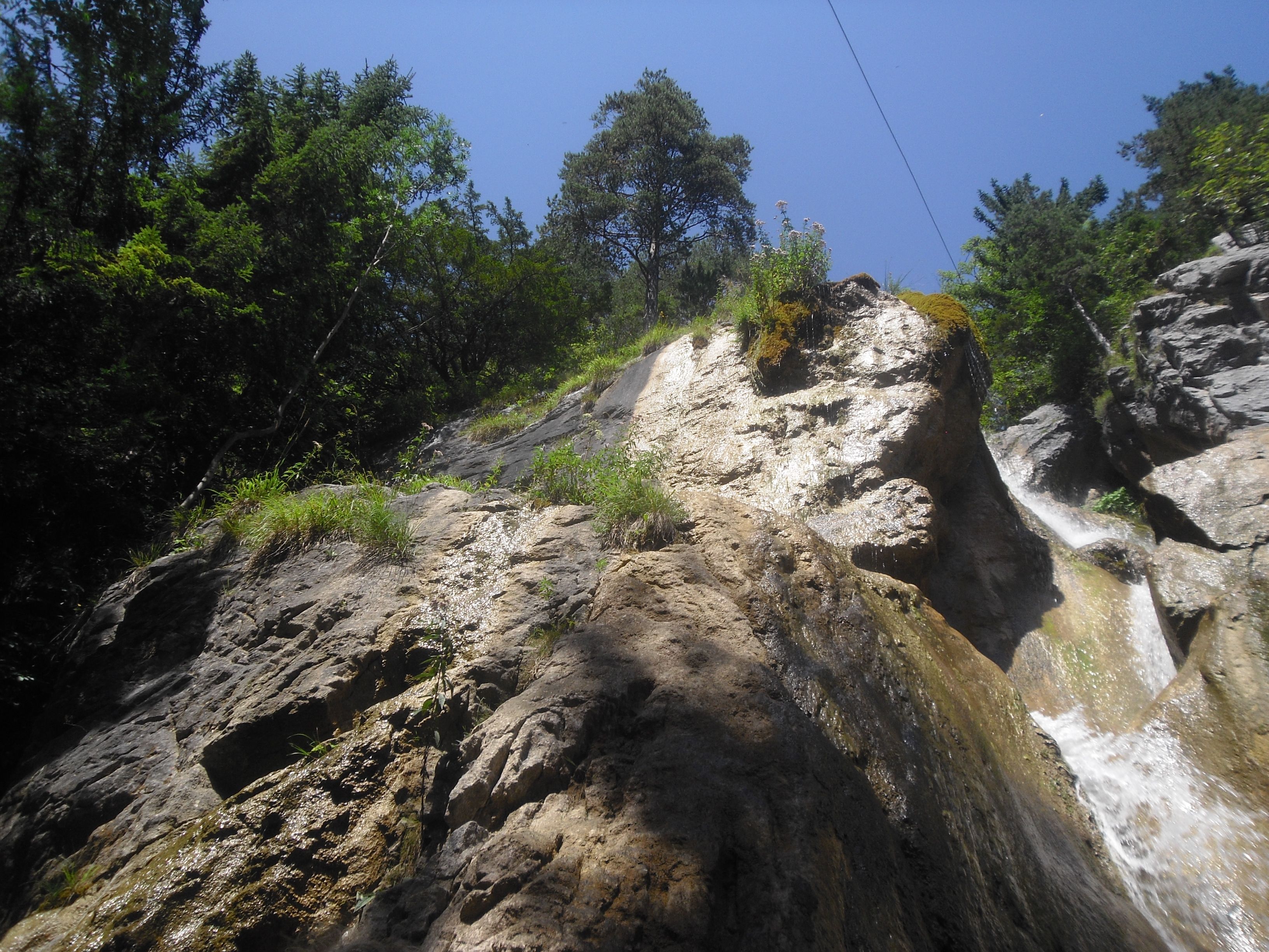 Felsiger Wasserfall mit Bäumen und blauem Himmel.