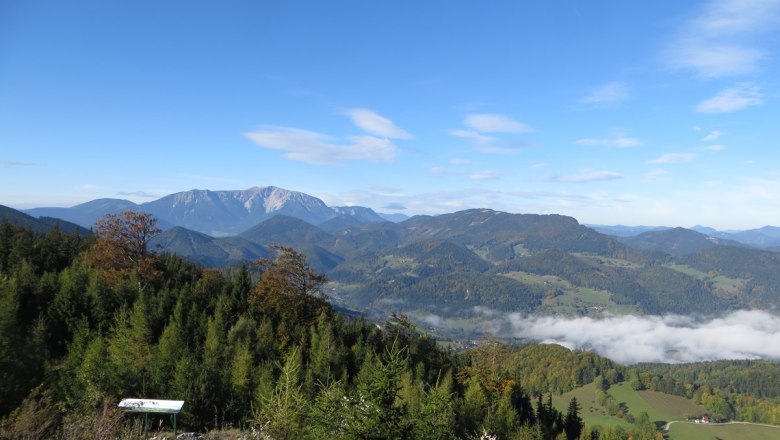 Panoramablick auf bewaldete H&uuml;gel und Berge unter blauem Himmel mit vereinzelten Wolken.